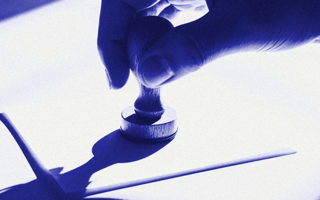 A hand pressing a rubber stamp onto a sheet of paper.