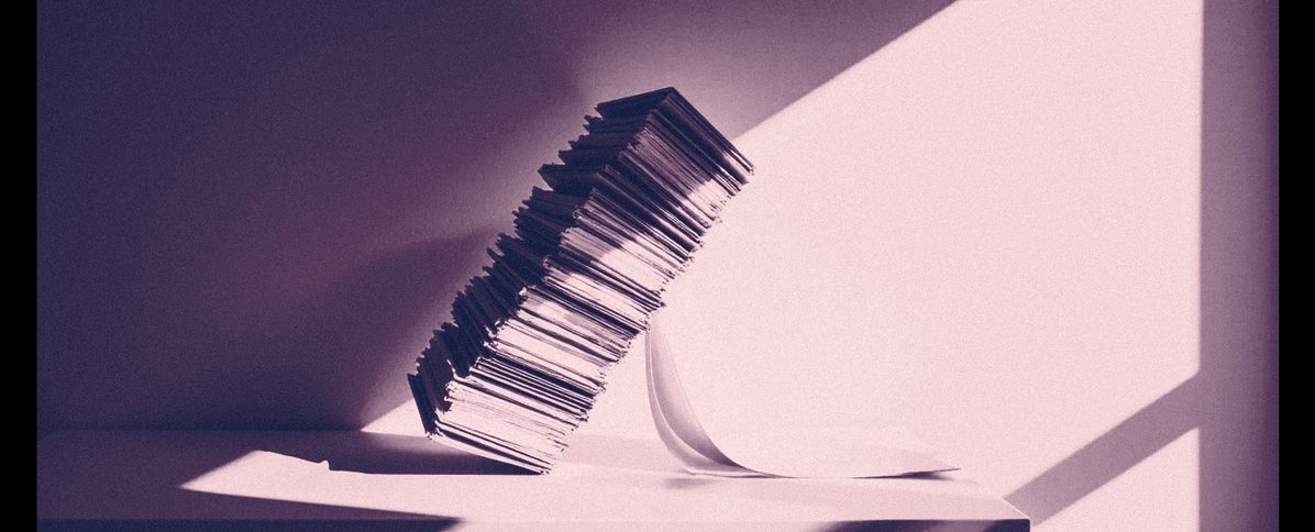 A tall stack of paper leaning and starting to topple.