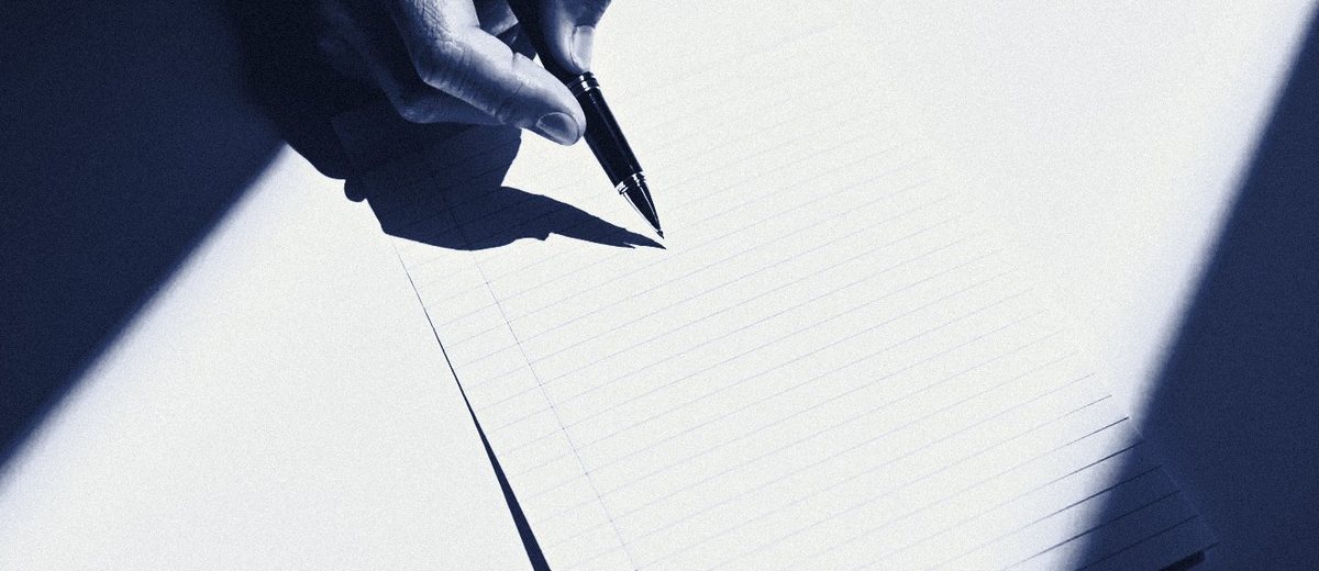 A hand touching a fountain pen to a blank ruled pad.